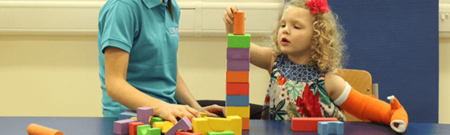 Child stacking blocks with her hand in a CIMT cast